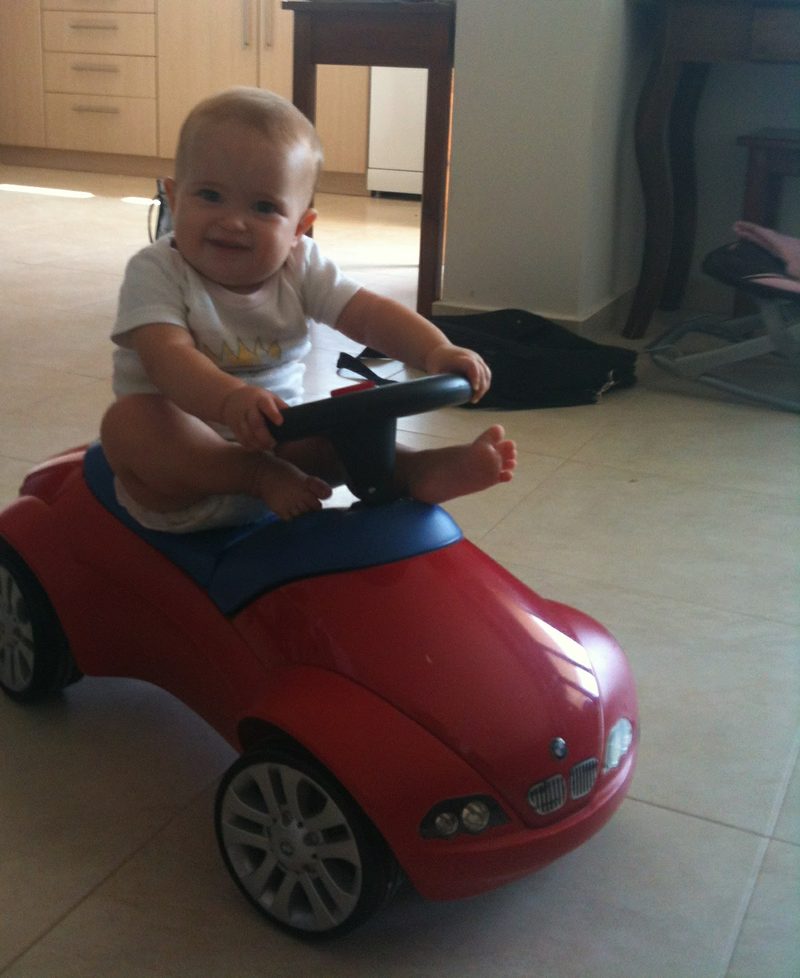 Baby sitzt mit sechs Monaten auf einem Rutschauto